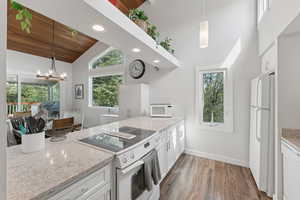 Kitchen featuring white appliances, lofted ceiling, wood finished floors, plenty of natural light, and light stone counters