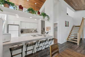 Kitchen with white appliances, high vaulted ceiling, wood ceiling, a kitchen breakfast bar, and white cabinetry