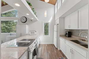 Kitchen featuring white appliances, backsplash, white cabinetry, light stone countertops, and light wood finished floors