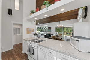 Kitchen featuring white appliances, white cabinetry, light stone countertops, hanging light fixtures, and healthy amount of natural light