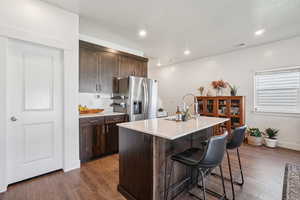 Kitchen with dark brown cabinetry, a breakfast bar area, a center island with sink, dark wood finished floors, and recessed lighting