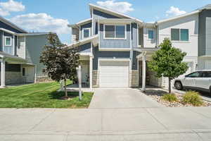 View of front of house with concrete driveway, a garage, stone siding, board and batten siding, and a front lawn
