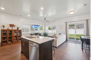 Kitchen featuring dark brown cabinetry, stainless steel dishwasher, dark wood-type flooring, light stone counters, and open floor plan