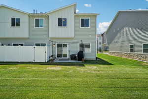 Back of house with board and batten siding, a patio, a lawn, and a gate