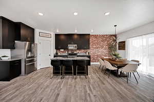 Kitchen featuring pendant lighting, light stone countertops, dark cabinets, appliances with stainless steel finishes, and a breakfast bar
