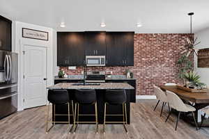 Kitchen with light stone countertops, a kitchen bar, a kitchen island with sink, brick wall, and appliances with stainless steel finishes