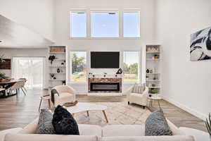 Living room with a high ceiling, wood finished floors, a fireplace, and built in shelves