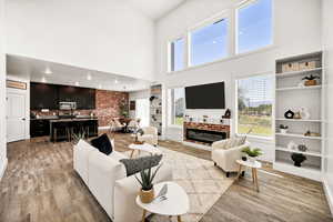 Living area with a high ceiling, light wood-type flooring, and a brick fireplace