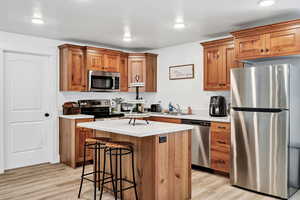 Kitchen featuring appliances with stainless steel finishes, a breakfast bar area, light countertops, light wood-style flooring, and a center island