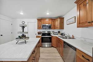 Kitchen featuring appliances with stainless steel finishes, brown cabinetry, light countertops, light wood-type flooring, and a kitchen island