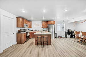 Kitchen with brown cabinets, stainless steel appliances, a kitchen island, a breakfast bar, and light countertops