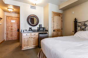 Bedroom featuring a textured wall, stainless steel fridge, and dark colored carpet