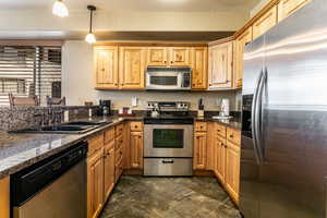 Kitchen with stainless steel appliances, hanging light fixtures, dark stone countertops, and dark stone finish flooring