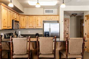 Kitchen featuring a breakfast bar, hanging light fixtures, stainless steel appliances, light brown cabinets, and a textured ceiling
