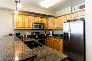 Kitchen with appliances with stainless steel finishes, pendant lighting, a textured wall, dark stone countertops, and a peninsula
