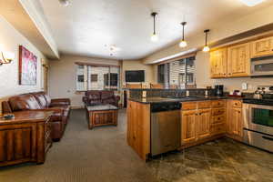 Kitchen with stainless steel appliances, open floor plan, decorative light fixtures, dark stone counters, and a textured wall