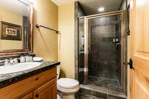 Full bathroom featuring a textured wall, vanity, a textured ceiling, a stall shower, and dark tile patterned floors