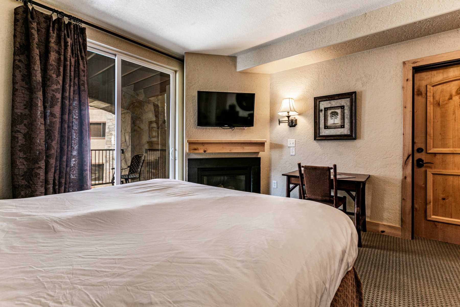 Bedroom featuring a textured wall, access to outside, a glass covered fireplace, a textured ceiling, and carpet flooring