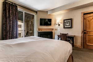Bedroom featuring a textured wall, access to outside, a glass covered fireplace, a textured ceiling, and carpet flooring