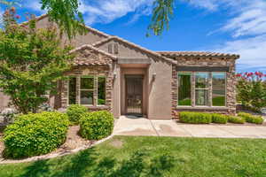View of exterior entry with stone siding, a yard, stucco siding, and a tile roof