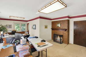 Carpeted office space featuring a brick fireplace and ornamental molding