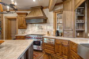 Kitchen featuring brown cabinetry, backsplash, premium range, a warming drawer, and ornamental molding