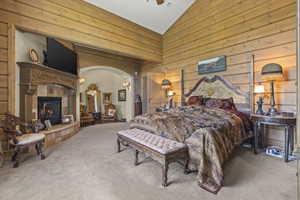 Bedroom with carpet, wooden walls, high vaulted ceiling, and a fireplace