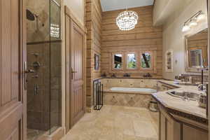 Bathroom with a stall shower, a bath, vanity, stone tile floors, and a chandelier