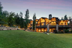 Rear view of property featuring a lawn, a balcony, a chimney, and stone siding