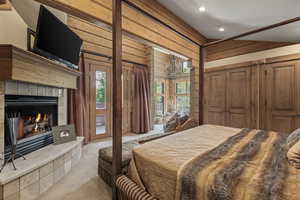 Carpeted bedroom featuring wood walls, a tile fireplace, lofted ceiling, a chandelier, and recessed lighting