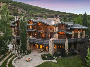 Rear view of house featuring a fire pit, stone siding, a chimney, a balcony, and a forest view