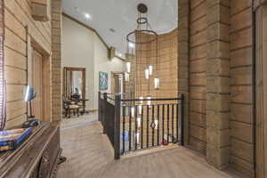 Corridor featuring wooden walls, crown molding, carpet floors, high vaulted ceiling, and an upstairs landing