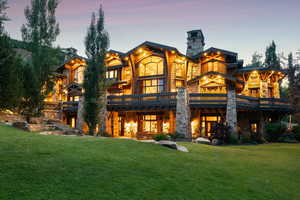 Back of house featuring stone siding, a balcony, a yard, and a chimney