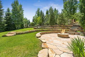 View of green lawn with a patio area, an outdoor fire pit, and stairway