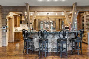 Bar area with brown cabinetry, wooden walls, dark wood finished floors, a chandelier, and pendant lighting