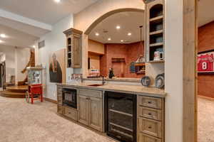 Indoor wet bar featuring glass insert cabinets, light colored carpet, wine cooler, black microwave, and recessed lighting