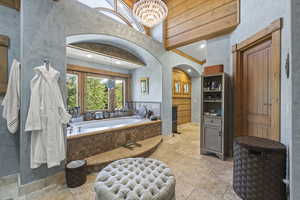 Full bath featuring stone tile floors, a garden tub, a chandelier, a closet, and recessed lighting