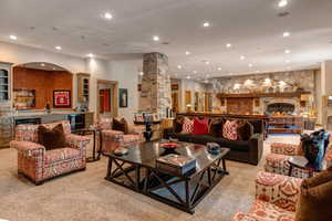 Living area with bar, decorative columns, recessed lighting, a stone fireplace, and light carpet