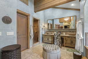 Bathroom featuring stone tile flooring, vanity, a stall shower, vaulted ceiling, and two sinks