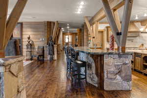 Kitchen featuring dark wood-style flooring, open shelves, wood walls, dark stone countertops, and a breakfast bar