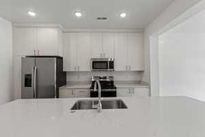 Kitchen with appliances with stainless steel finishes, light stone countertops, and recessed lighting