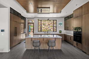 Kitchen featuring a raised ceiling, a kitchen island, a breakfast bar, oven, and wooden ceiling