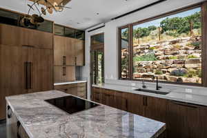 Kitchen with black electric stovetop, a center island, light stone countertops, and modern cabinets