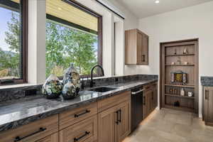Kitchen featuring open shelves, dark stone counters, brown cabinets, and black dishwasher