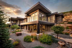 Rear view of property featuring stone siding, a patio, and a balcony