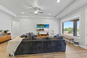 Living room featuring a tray ceiling, light wood finished floors, a ceiling fan, and recessed lighting