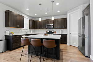 Kitchen with pendant lighting, a breakfast bar, a center island, appliances with stainless steel finishes, and dark brown cabinetry