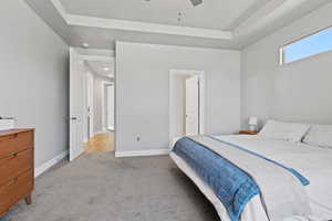 Bedroom with light colored carpet, a raised ceiling, and a ceiling fan