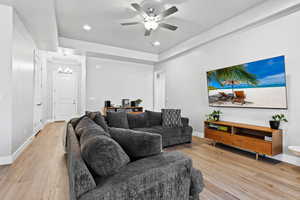 Living room with light wood-type flooring, a raised ceiling, a chandelier, recessed lighting, and ceiling fan