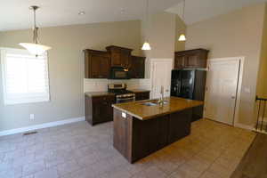 Kitchen featuring dark brown cabinets, backsplash, gas stove, dark stone counters, and high vaulted ceiling